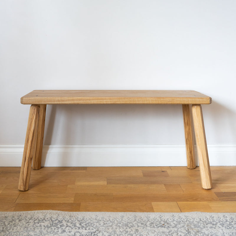 Ash bench against an off-white wall.