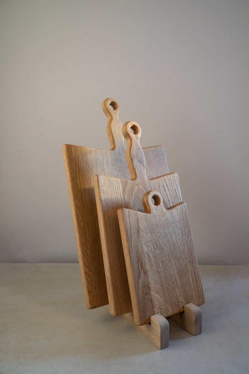 Three oak chopping boards with handles in a stand against a neutral background