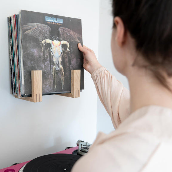 Woman takes an Eagles record from an oak record rack.