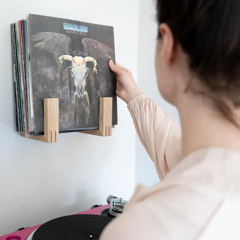 Woman takes an Eagles record from an oak record rack.
