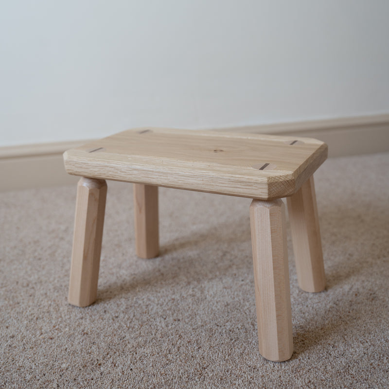 Wooden stool on a carpeted floor with a plain wall background