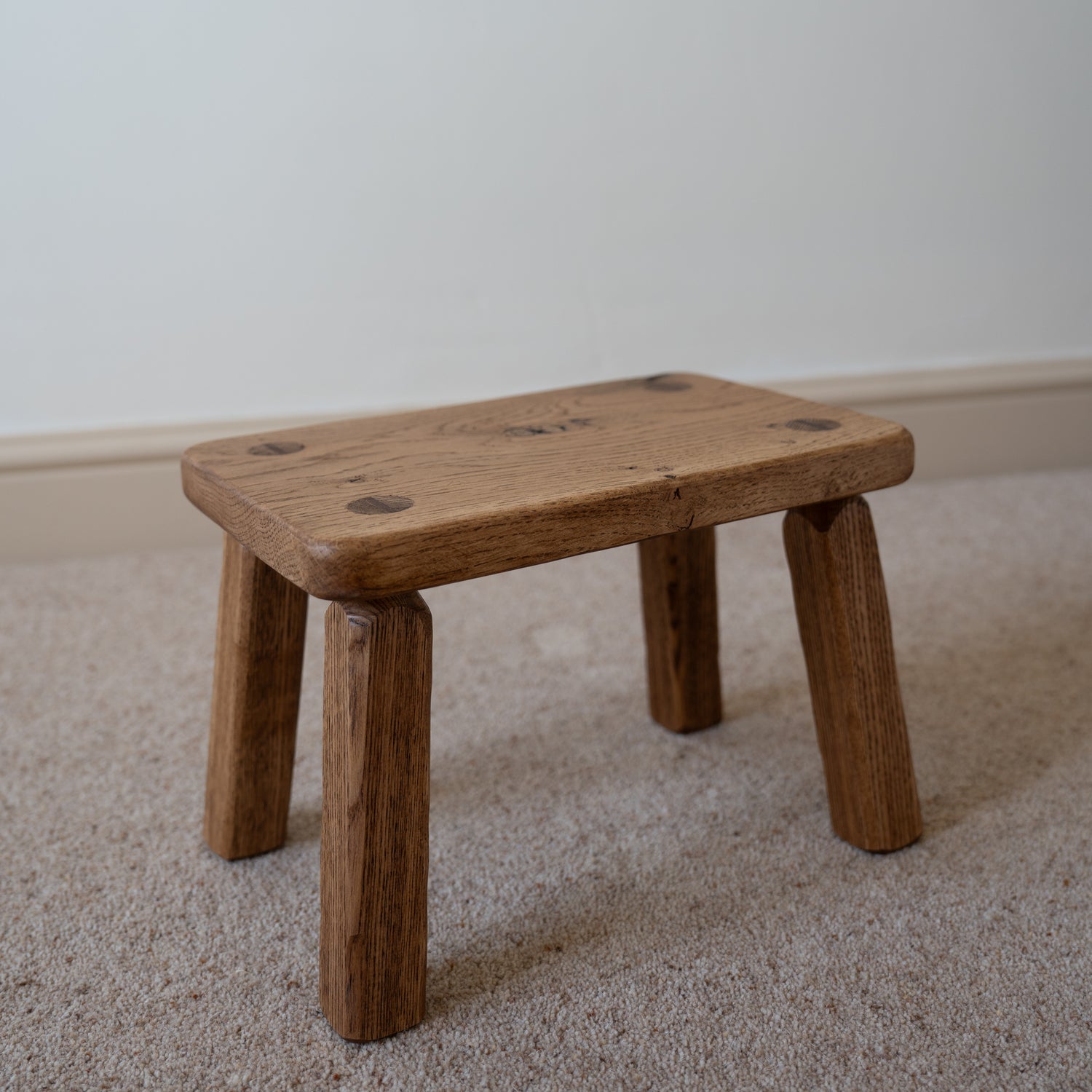 Small wooden stool on a carpeted floor with a plain wall background